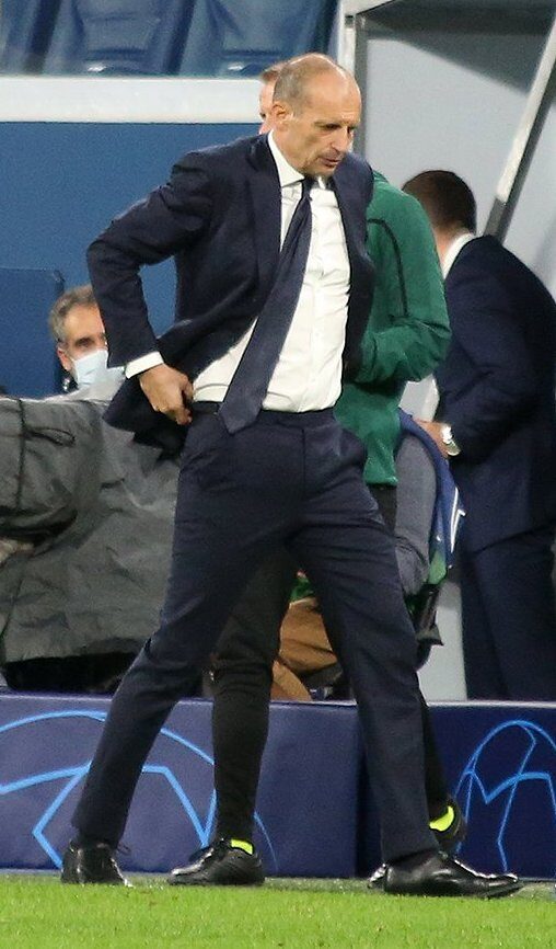 Massimiliano Allegri, wearing a dark suit and tie, stands on the touchline gesturing during a Champions League match while he was Juventus head coach.