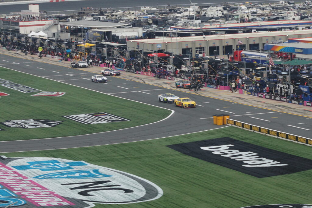 NASCAR Cup Series crew performing a pit stop during a race, cars lined along pit road.
