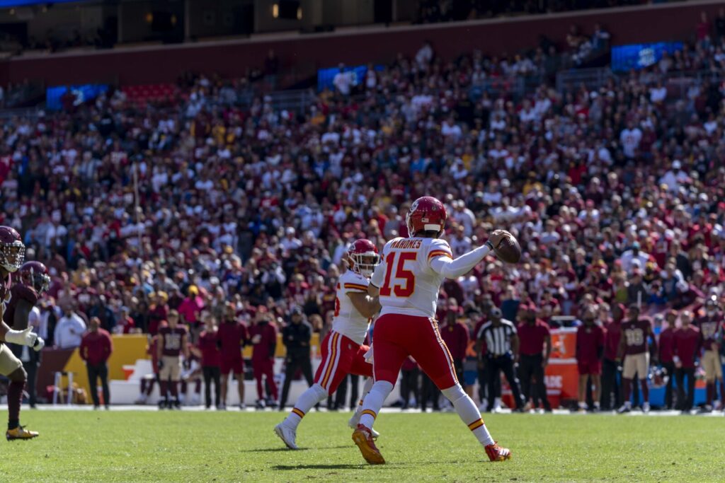 An NFL quarterback in a white jersey throws a pass on the run during a game.