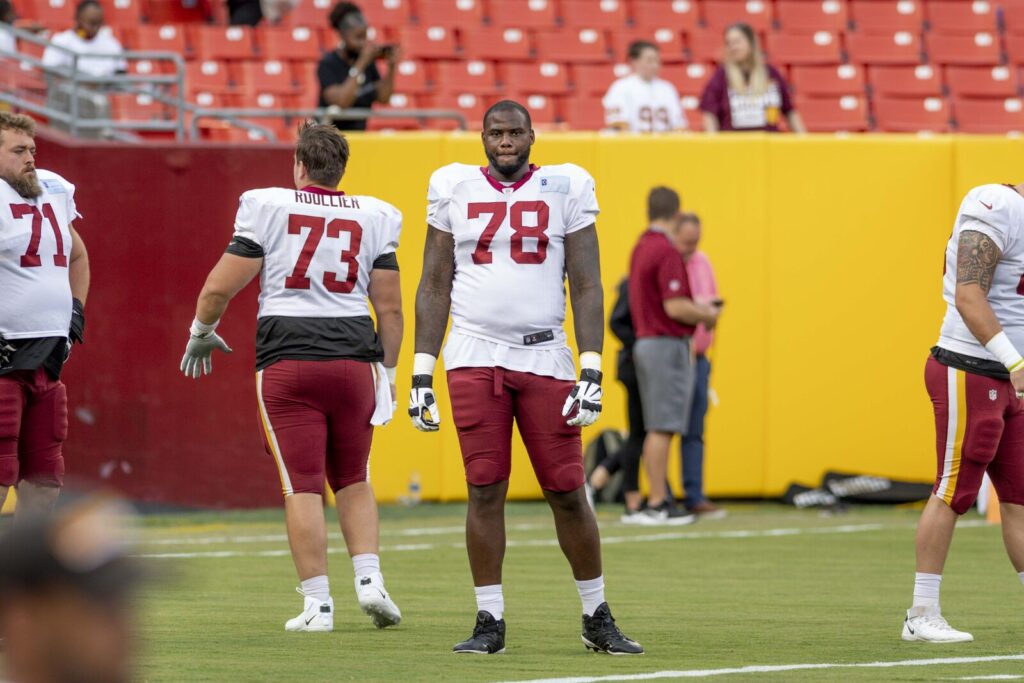 Washington Football Team offensive linemen in full pads and helmets during an NFL training camp practice session.