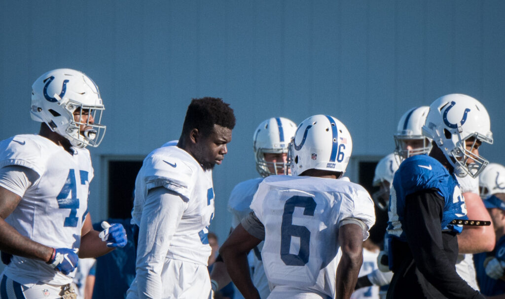 NFL players in helmets and pads gather on the field during a training camp practice