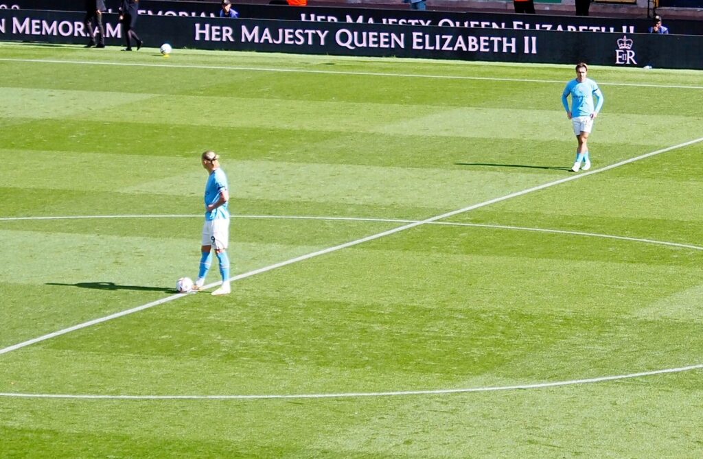 Erling Haaland lines up to kick off with Jack Grealish in the background, both in Manchester City kit, ahead of a 2022 Premier League match against Wolverhampton Wanderers.