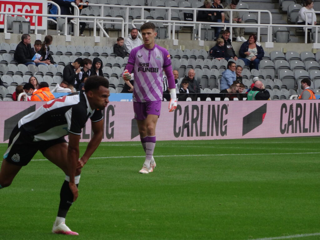 Newcastle United players warm up on the pitch at St James Park before a Premier League match, shirt sponsor branding visible on the goalkeeper kit.