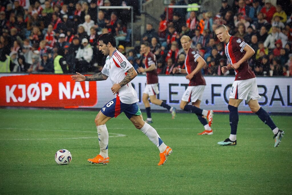 Sandro Tonali, wearing the number 8 shirt for Italy, dribbles the ball forward during a match against Norway as opposing players give chase.