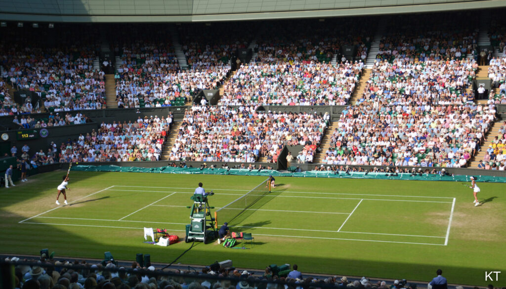 Two tennis players competing on Wimbledon Centre Court, with a packed crowd in the stands behind them.