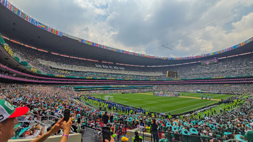 A packed Estadio Azteca in Mexico City during the FIFA World Cup 2026 opening match, with fans filling every tier below a ring of national flags.