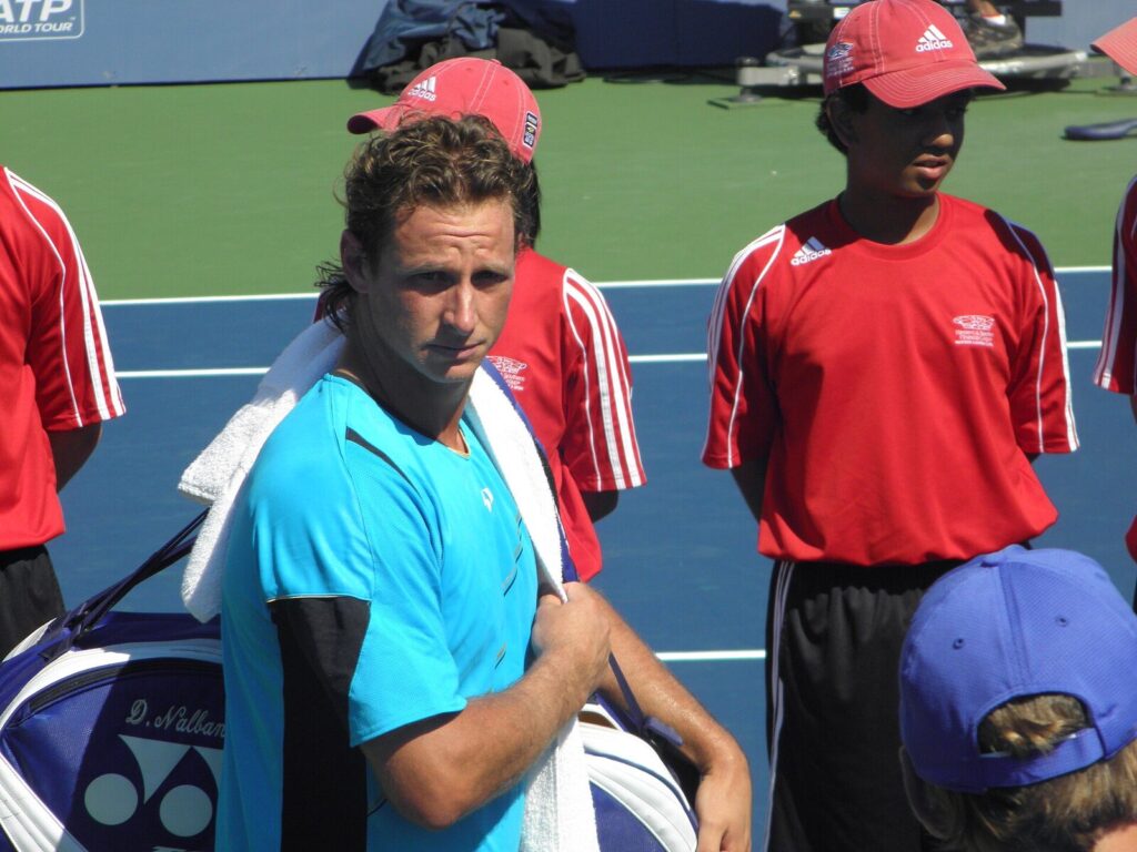 David Nalbandian on court at the 2010 Western & Southern Open in Cincinnati, holding a towel and racket bag beside ballkids in red