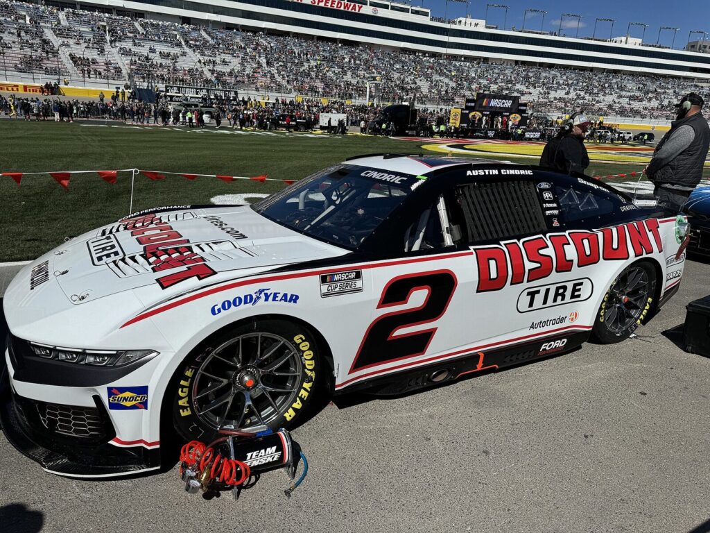 Austin Cindric's white and red No. 2 Discount Tire Ford Cup car parked on pit road in front of grandstands, crew members standing nearby. (File photo: Austin Cindric's car at the 2024 Pennzoil 400 in Las Vegas, not from the Daytona regular-season finale.)
