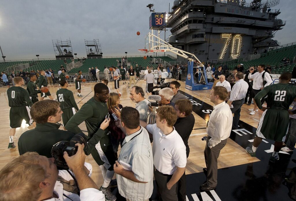 Draymond Green, wearing a Michigan State jersey, is interviewed by reporters courtside during a college basketball practice aboard the USS Carl Vinson in 2011.
