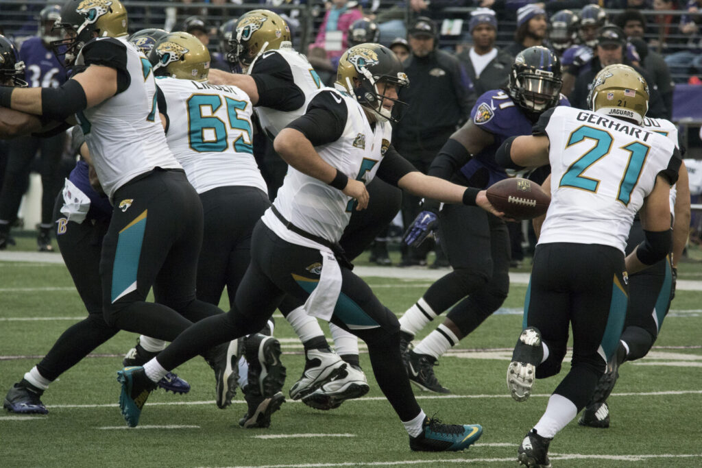 NFL offensive players executing a handoff during a game, with defenders closing in on the field.