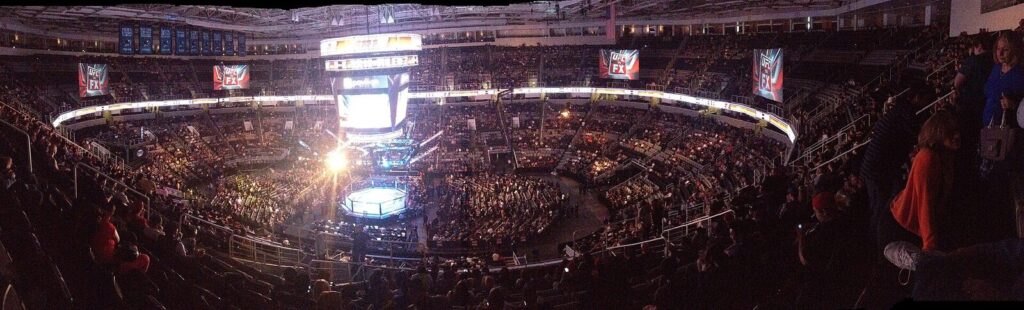 Wide shot of a packed arena during a UFC event with the octagon lit up at the center (Foto de arquivo: público durante um evento do UFC (UFC on FX), imagem genérica não ligada a um card ou ranking específico.)